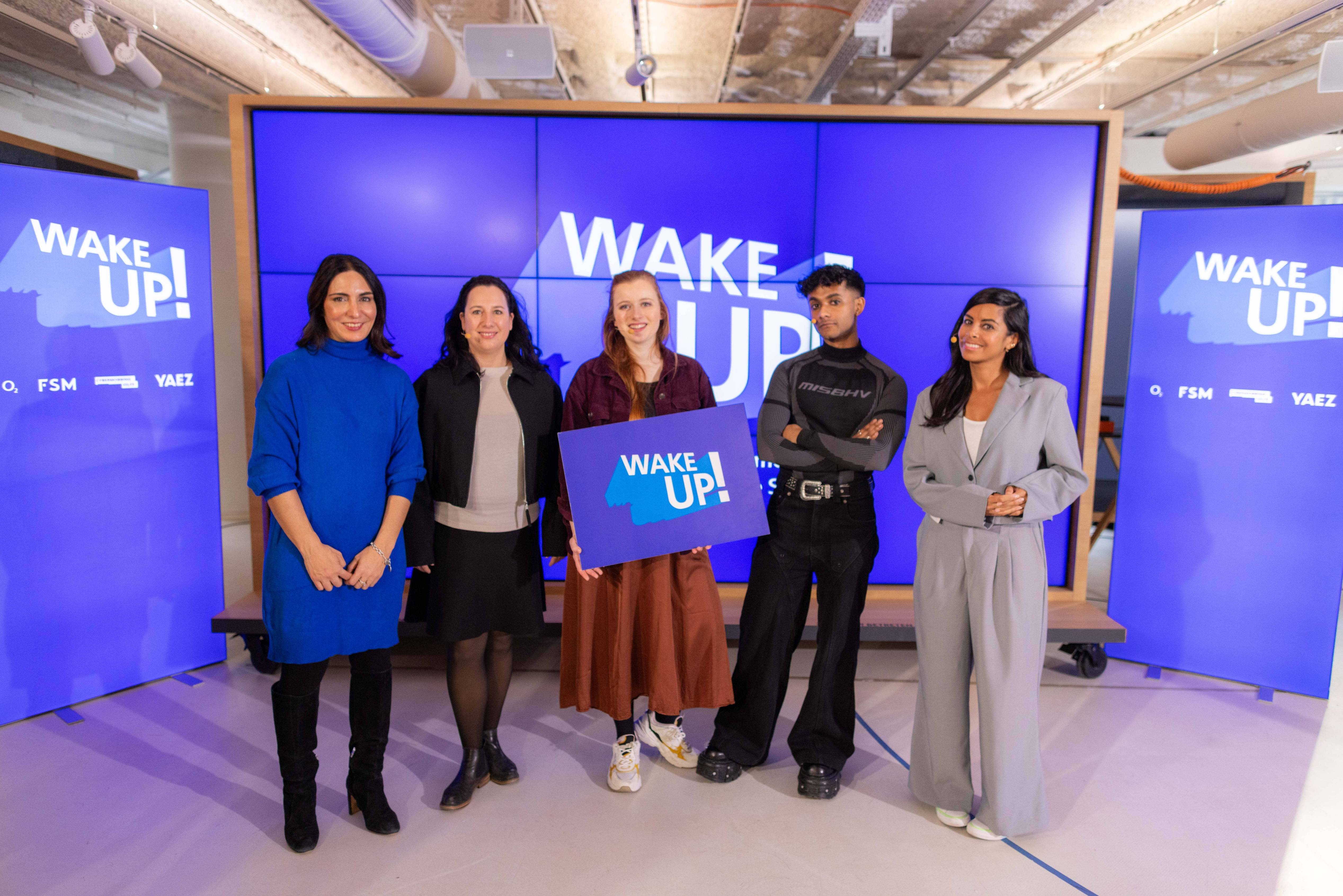 Vor einer digitalen Wand stehen die Gäste und halten ein WAKE UP Schild hoch