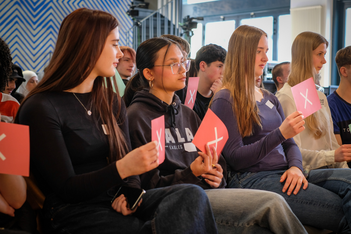 Schüler:innen halten ein rotes Schild mit einem X darauf hoch.