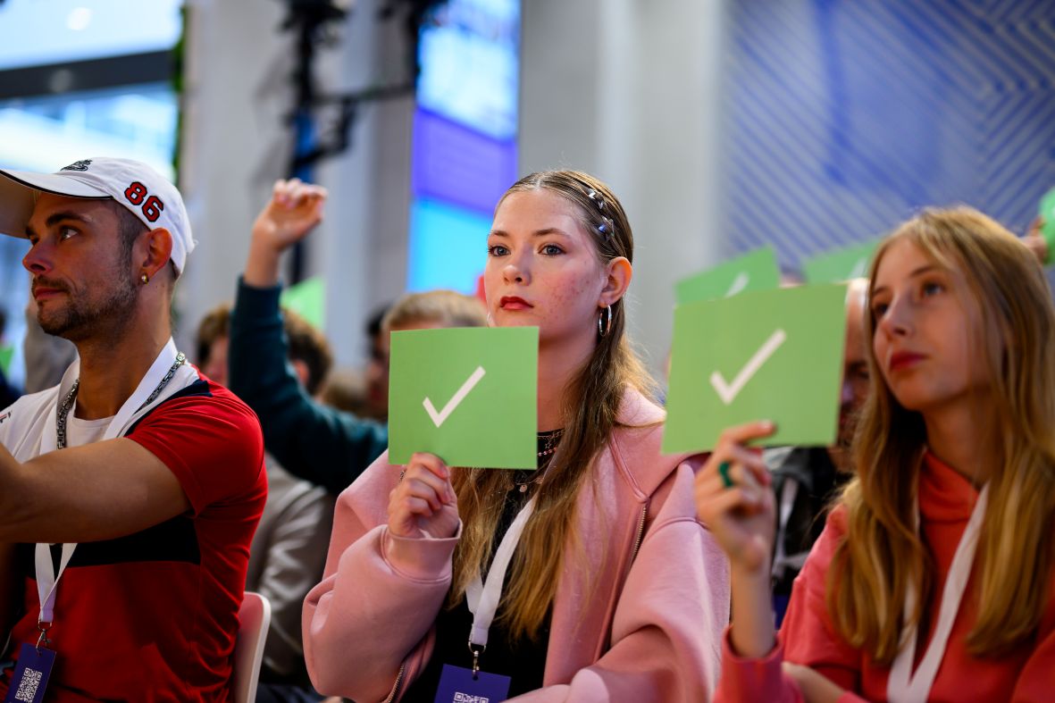 Teilnehmende im Publikum halten grünes Schild hoch